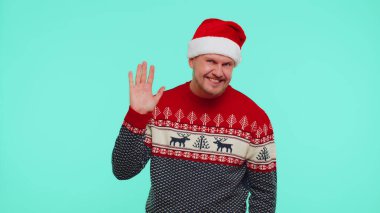 Kırmızı Noel süveteri giyen adam el sallayarak el sallıyor. Yeni yılı kutlamak için birine hoş geldin diyor.