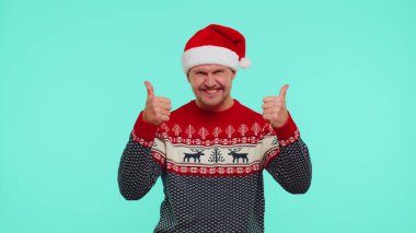 Komik adam kırmızı yeni yıl süveteri giyiyor. Başparmak kaldırıyor. Mavi arka plan gibi güzel bir şeye katılıyor.