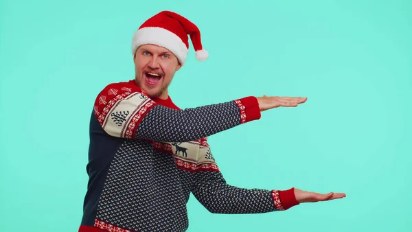 Мужчина носит красный новогодний свитер олень показывающий большие пальцы вверх и указывающий на пустое рекламное место — стоковое фото