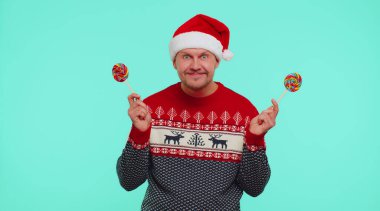 Kırmızı yeni yıl süveteri giyen komik bir adam, elinde şeker şeritli lolipoplar tutan, dans eden, aptal suratlar yapan