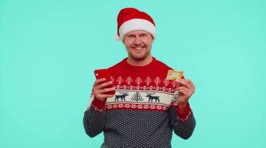 Noel kazaklı bir adam kredi kartı, akıllı telefon kullanarak internetten para alışverişi yapıyor.