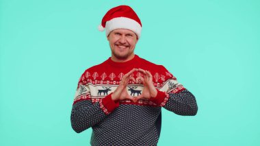 Noel süveteri içindeki gülümseyen adam kalp hareketi yapar. Aşk işareti iyi duygular ifade eder.