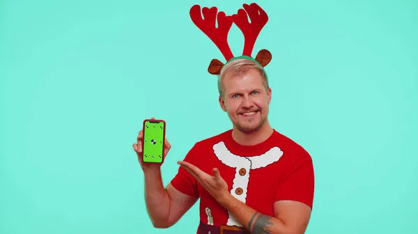 Homem de t-shirt Santa Christmas e chifres de veado mostrando telefone celular com chave de croma de tela verde — Fotografia de Stock