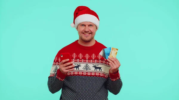 Чоловік у різдвяному светрі за допомогою кредитної банківської картки, смартфон під час переказу грошей через інтернет — стокове фото