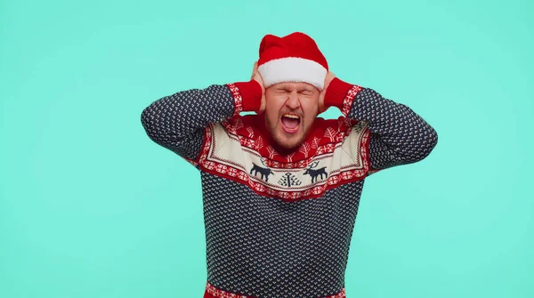 Чоловік у різдвяному светрі прикриває вуха і жестикулює ні, уникаючи поради ігноруючи неприємний шум — стокове фото