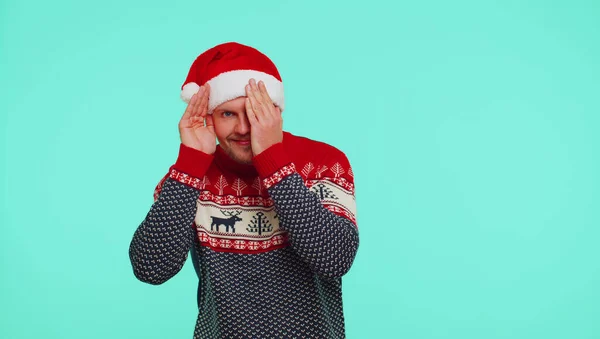 Чоловік у светрі Санта-різдвяний капелюх дуріє навколо, закриваючи очі рукою і шпигуючи через — стокове фото