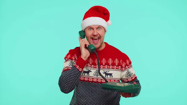 Смішний чоловік у різдвяному светрі, розмовляючи на провідному старовинному телефоні 80-х, каже: — стокове фото