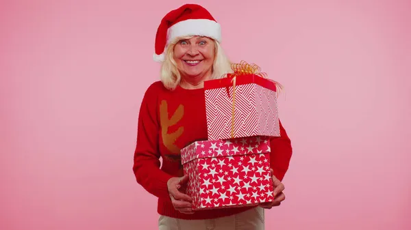 Старша бабуся на різдвяному светрі тримає багато подарунків на новорічному подарунковому ринку. — стокове фото