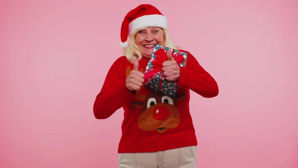 Бабушка в свитере Санта Рождество получает подарок коробку выражая удивление счастье — стоковое фото