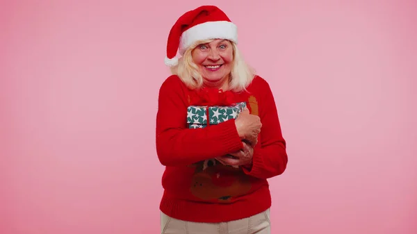 Літня старша прекрасна бабуся носить червоний новорічний светр і капелюх, посміхаючись дивиться на камеру — стокове фото