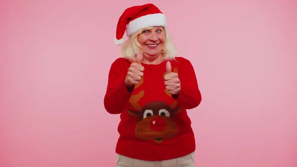 Бабуся носить червоний новорічний светр з оленями піднімає великі пальці вгору, погоджується з чимось хорошим, наприклад — стокове фото