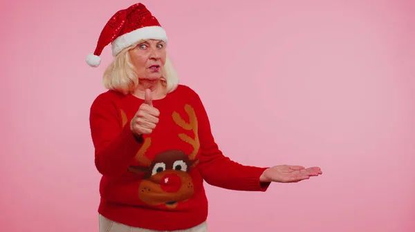 Бабуся в різдвяному светрі, показуючи великі пальці вгору і вказуючи на порожнє рекламне місце — стокове фото