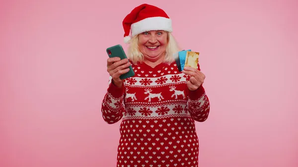 成熟したクリスマスの祖母の女性は携帯電話のプラスチック製のクレジットカードを使用しています。 — ストック写真