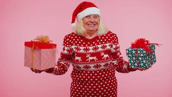 Бабушка в свитере Санты представляет одну рождественскую подарочную коробку, протягивает руки к камере — стоковое фото