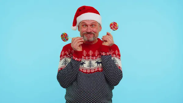 Homme drôle en pull de Noël rouge tenant des sucette rayées bonbons se cachant derrière eux en train de s'amuser — Photo