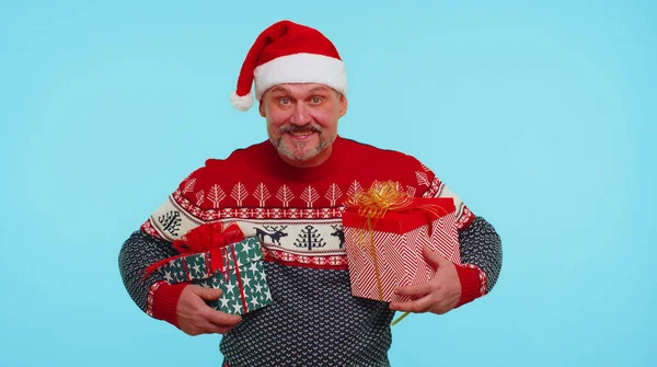 Wesoły mężczyzna w swetrze Mikołaja prezentuje dwa pudełka świąteczne, wyciąga ręce do kamery — Zdjęcie stockowe