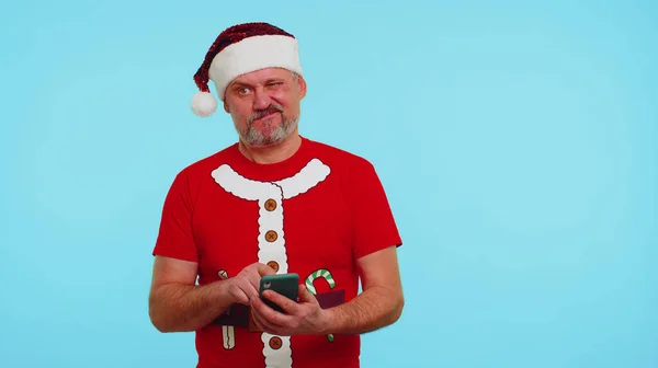 Homem de t-shirt de Natal, chapéu usando telefone celular digitando novo post na web, compras on-line, navegação — Fotografia de Stock