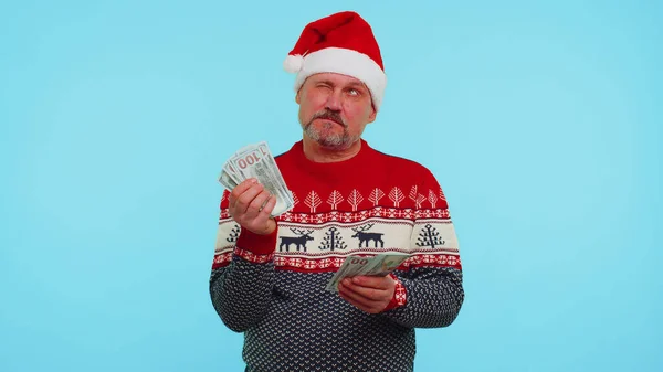 Багатий бізнесмен у різдвяному светрі тримає стопку грошових доларів готівкою думаючи, який подарунок купити — стокове фото