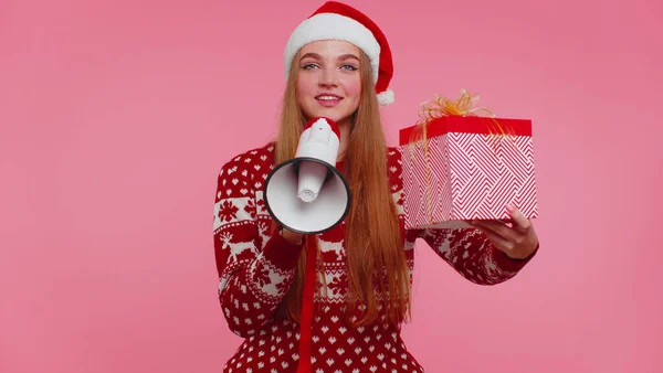 Дівчина в різдвяному светрі з подарунковою коробкою кричить в мегафоні оголошує про знижки продажу покупки — стокове фото