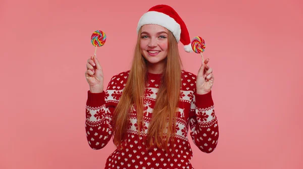 Menina engraçada em camisola de Ano Novo segurando pirulitos listrados doces escondidos atrás deles, brincando — Fotografia de Stock