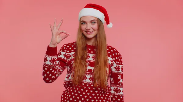 Доросла дівчина в різдвяному светрі дивиться на камеру, показуючи нормальний жест, як знак позитивний — стокове фото