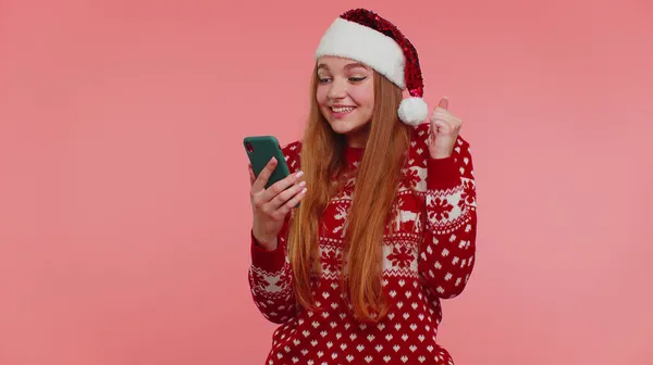 Доросла дівчина в червоному різдвяному светрі дивиться дисплей смартфона щиро радісно виграє успіх — стокове фото