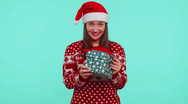 Весела дівчина в різдвяному светрі отримує подарункову коробку, висловлюючи враження щастя — стокове фото