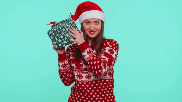 Радісна дівчина носить різдвяний святковий светр, який отримав подарунок, зацікавлений у тому, що всередині подарункової коробки — стокове фото