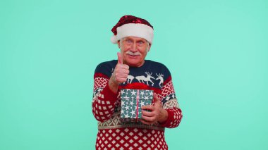 Grandfather in Santa sweater presenting one Christmas gift box, stretches out his hands to camera clipart