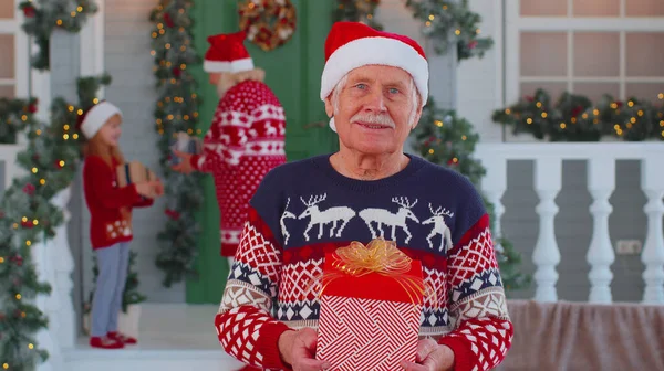 Портрет дідуся, який дарує подарунки, посміхаючись біля прикрашеного різдвяного будинку з родиною. — стокове фото