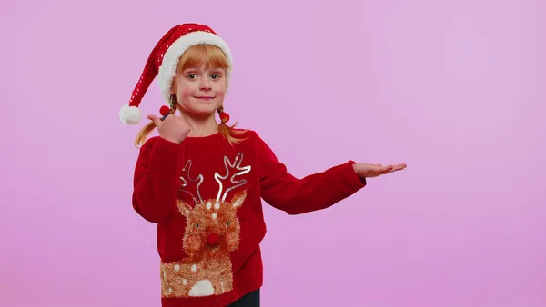 Дівчина в червоному новорічному светрі олень показує великі пальці вгору і вказує на порожній рекламний простір — стокове фото