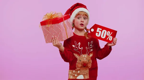 Criança menina em chapéu de Natal mostrando caixa de presente e 50% de desconto inscrições banner texto nota — Fotografia de Stock
