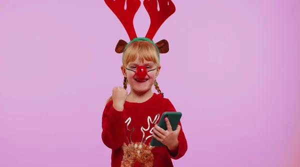 Enfant fille en bois de cerf de Noël regardant l'affichage du smartphone se réjouissant sincèrement gagner de la chance de succès — Photo