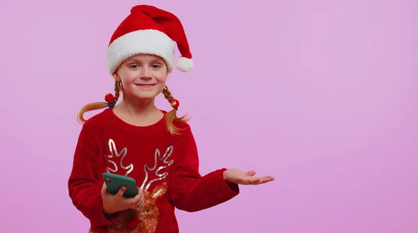 Menina criança no chapéu de Natal Santa com telefone celular mostrando apontando lugar vazio, área de publicidade — Fotografia de Stock