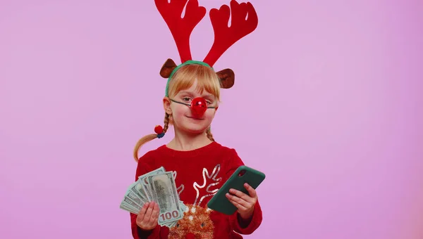 Дівчина в червоних різдвяних оленячих рогів дивиться смартфон радісно виграє успіх отримувати гроші — стокове фото