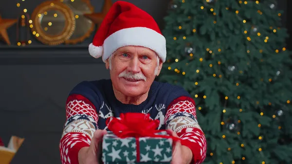 Senior Opa in Silvesterpullover und Hut präsentiert Weihnachtsgeschenkbox, Urlaub zu Hause — Stockfoto