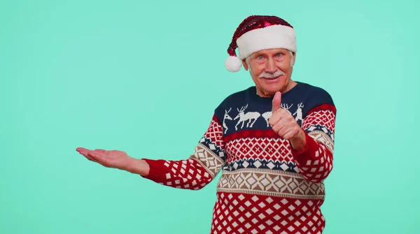 Дедушка в рождественском свитере Санта показывает большие пальцы вверх и указывая пустое место, рекламная площадь — стоковое фото