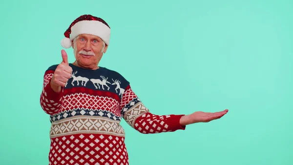 爷爷穿着圣诞鹿毛衫，竖起大拇指，指着空白的广告空间 — 图库照片