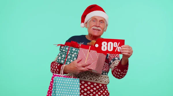 Дідусь у різдвяному светрі, що показує подарункову коробку та 80 відсотків дисконтних написів текст банера — стокове фото