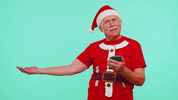Дід Санта Різдвяна футболка з мобільним телефоном, що вказує на порожнє місце, рекламну зону — стокове фото