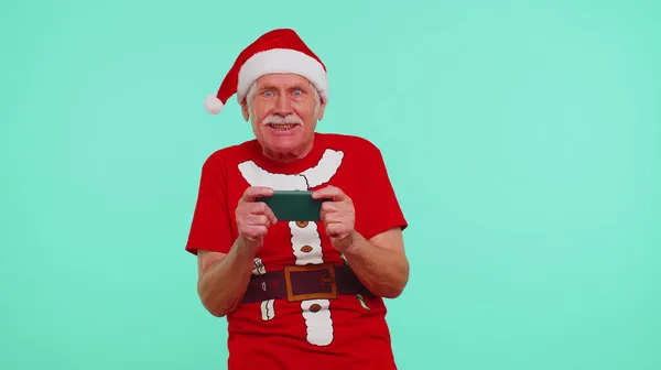 Worried grandfather in Christmas t-shirt enthusiastically playing racing video games on mobile phone — Stock Photo, Image