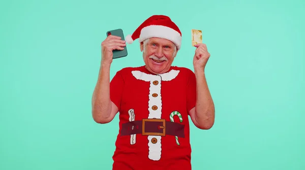 Зрілий Різдвяний дід використовує мобільний телефон, пластикову кредитну банківську картку, перемагає, вау — стокове фото