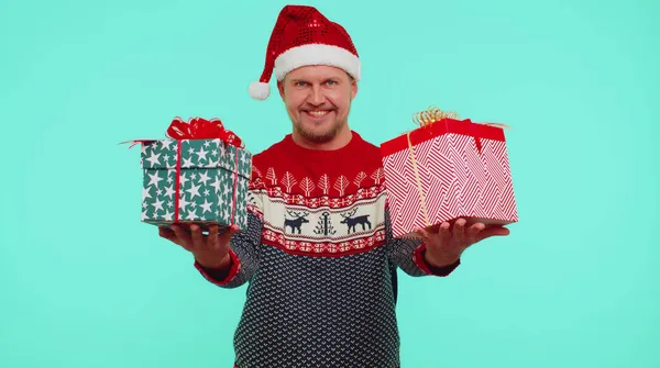 Чоловік носить червоний Новий рік, представляючи різдвяні подарункові коробки, розтягує руки до камери посміхаючись — стокове фото
