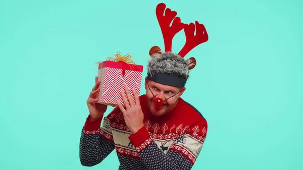 Homem engraçado usa chifres de veado de camisola de Ano Novo recebido presente, interessado em que dentro da caixa de presente — Fotografia de Stock