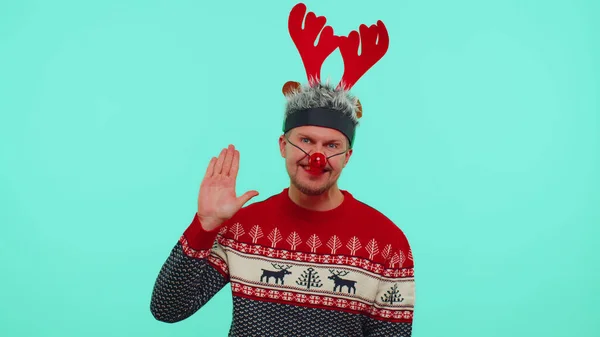 Homem positivo em camisola de Natal, chifres de veado ondas mão palma em Olá gesto recebe alguém — Fotografia de Stock