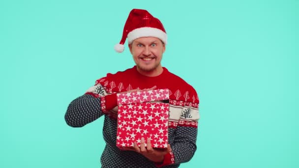 Divertido 30s años viejo hombre usa rojo año nuevo suéter sombrero desenvolver regalo, apertura caja con gato mascota — Vídeos de Stock