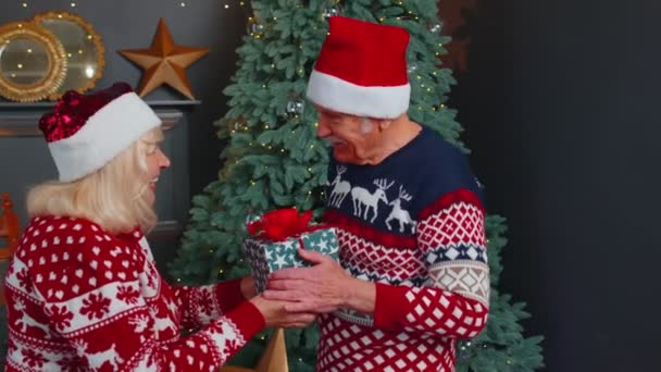 장식된 거실에서 할아버지를 놀라게 한 할머니가 크리스마스 선물 상자를 제공하는 모습 — 비디오