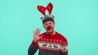 Noel süveteri giymiş pozitif bir adam, geyik boynuzları, el sallıyor.