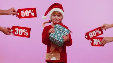 Küçük kız elinde hediye kutuları tutuyor ve Noel indirimleri alıyor. Yazılar, afişler.