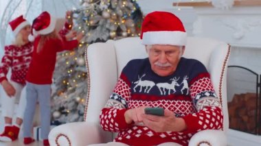 Yaşlı büyükbaba Noel hediyesi alıyor. Evde cep telefonuyla alışveriş yapıyor.